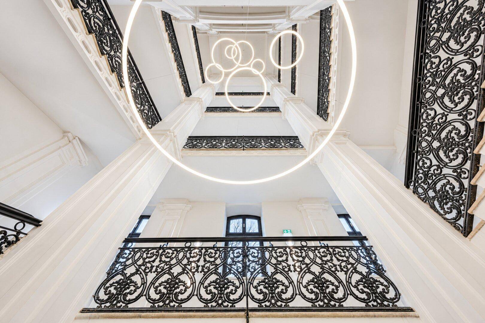 Beeindruckendes Treppenhaus mit kunstvollem Geländer und modernen, ringförmigen Deckenleuchten.