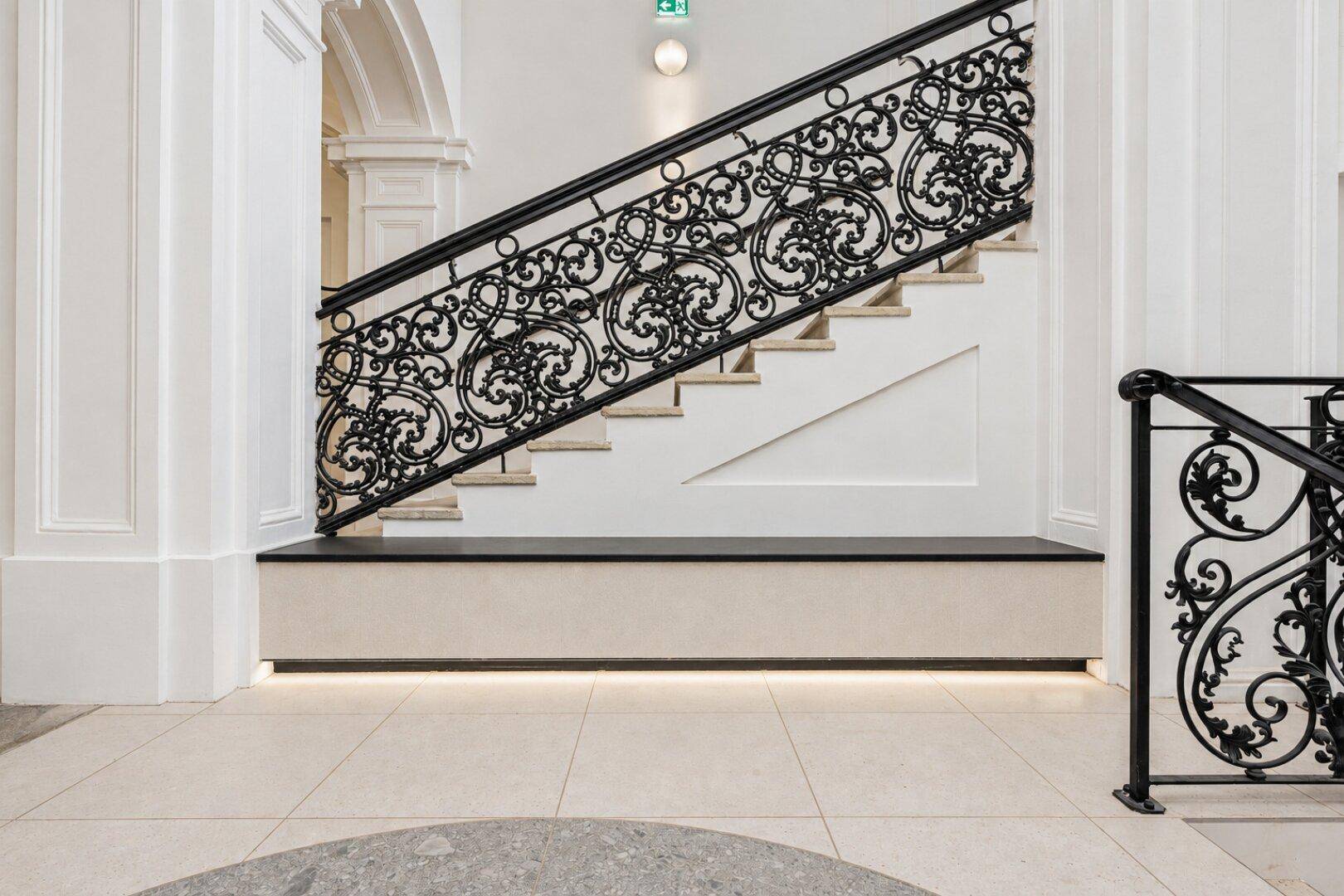Detailansicht der eleganten Treppe mit schmiedeeisernem Geländer und heller Beleuchtung im Eingangsbereich.
