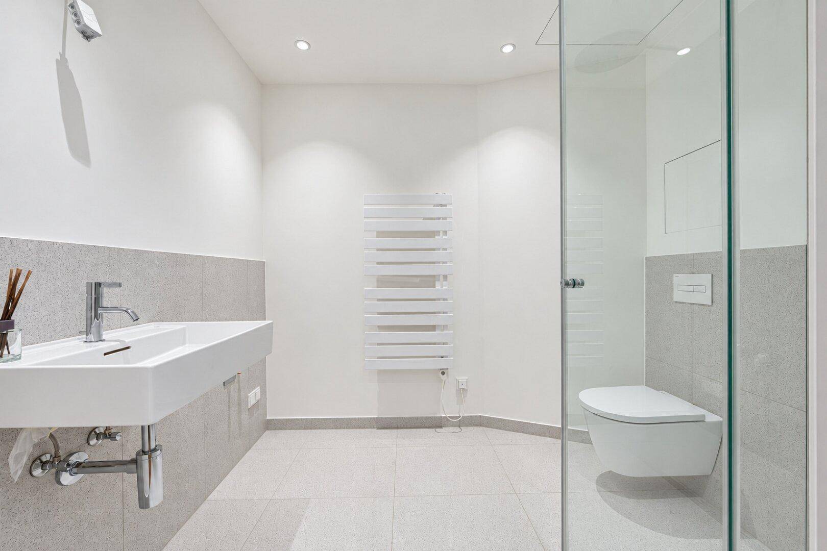 Modernes Badezimmer mit großer Dusche, wandhängendem WC und beheiztem Handtuchhalter.