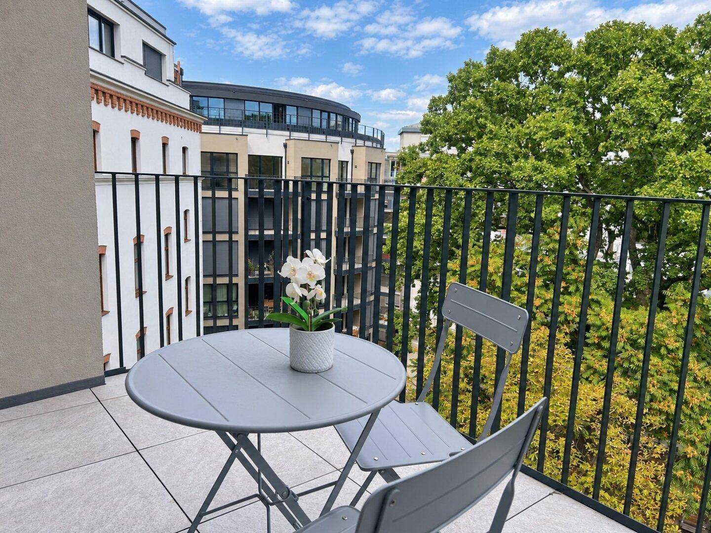 Gemütlicher Balkon mit Sitzgelegenheiten und Blick auf umliegende Gebäude und Bäume.