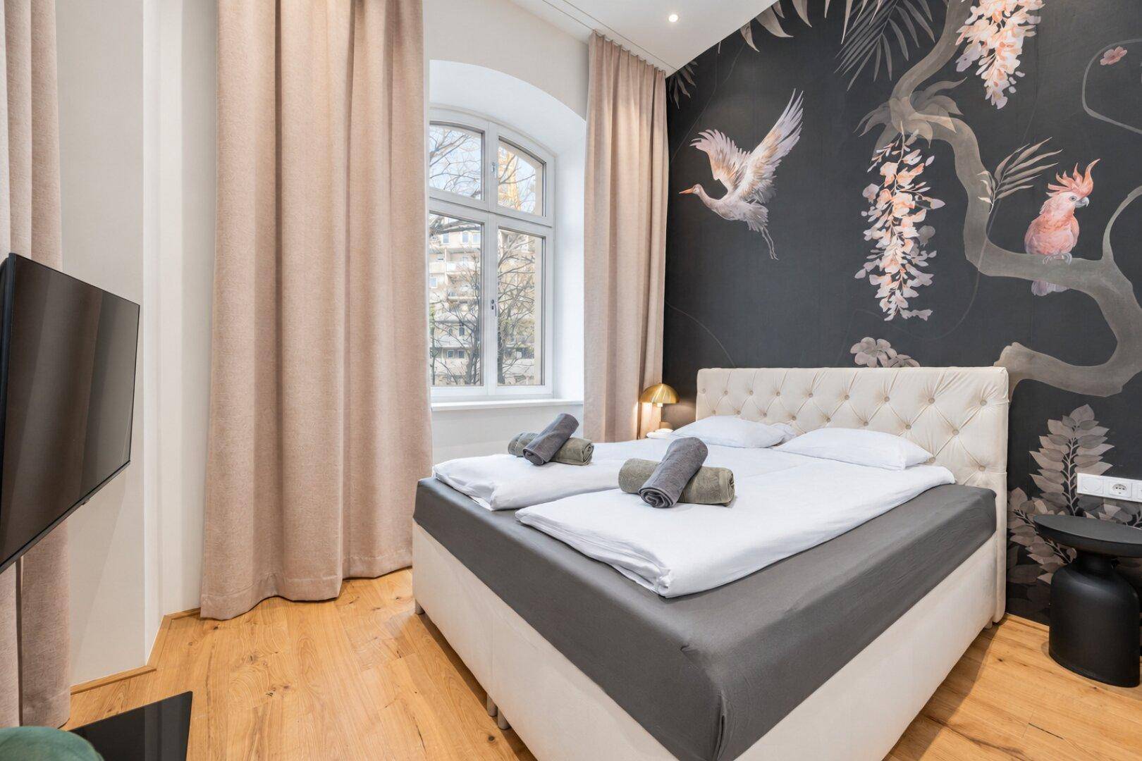 Schlafzimmer mit Doppelbett, Fernseher und einer auffälligen Wandtapete mit Vogelmotiv.