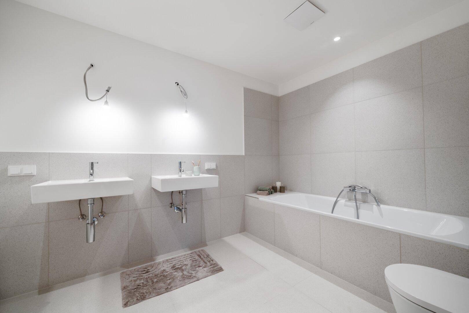 Modernes Badezimmer mit zwei Waschbecken, Badewanne und hellen Fliesen an den Wänden.
