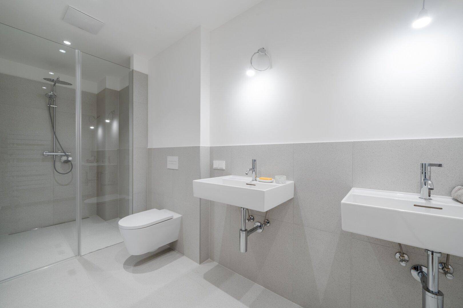 Geräumiges Badezimmer mit ebenerdiger Dusche, Wand-WC und zwei modernen Waschbecken.