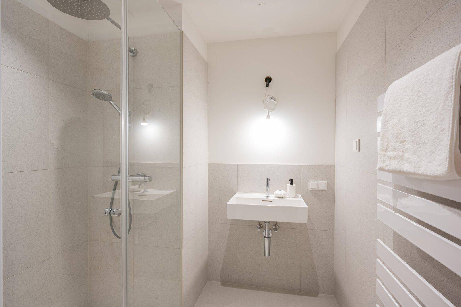 Modernes Badezimmer mit ebenerdiger Dusche, Wandwaschbecken und beheiztem Handtuchhalter.