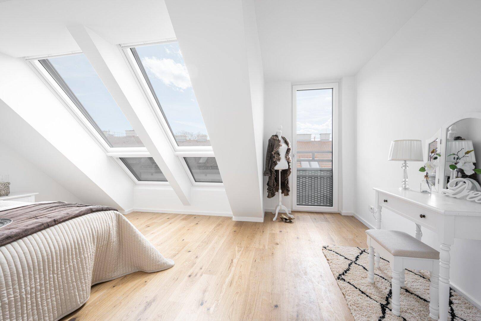 Helles Schlafzimmer im Dachgeschoss mit Holzboden, Dachfenstern und Zugang zum Balkon.