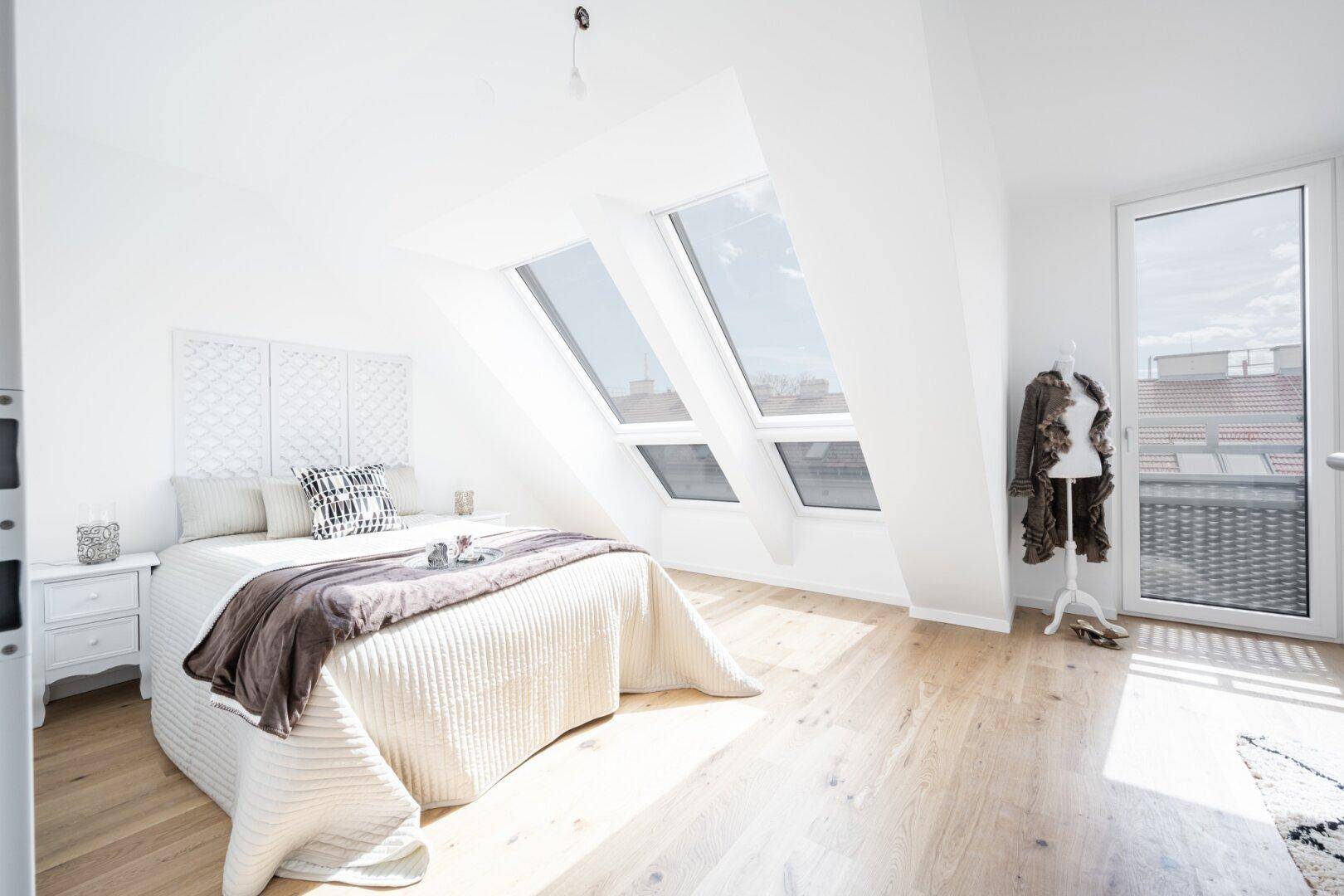 Modernes Schlafzimmer mit Holzboden, Dachfenstern und einem bequemen Bett in heller Atmosphäre.