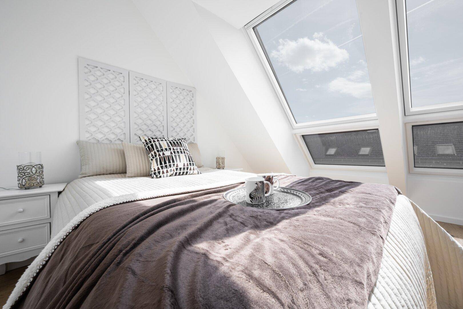 Gemütliches Schlafzimmer mit weicher Bettwäsche und viel Tageslicht durch die Dachfenster.