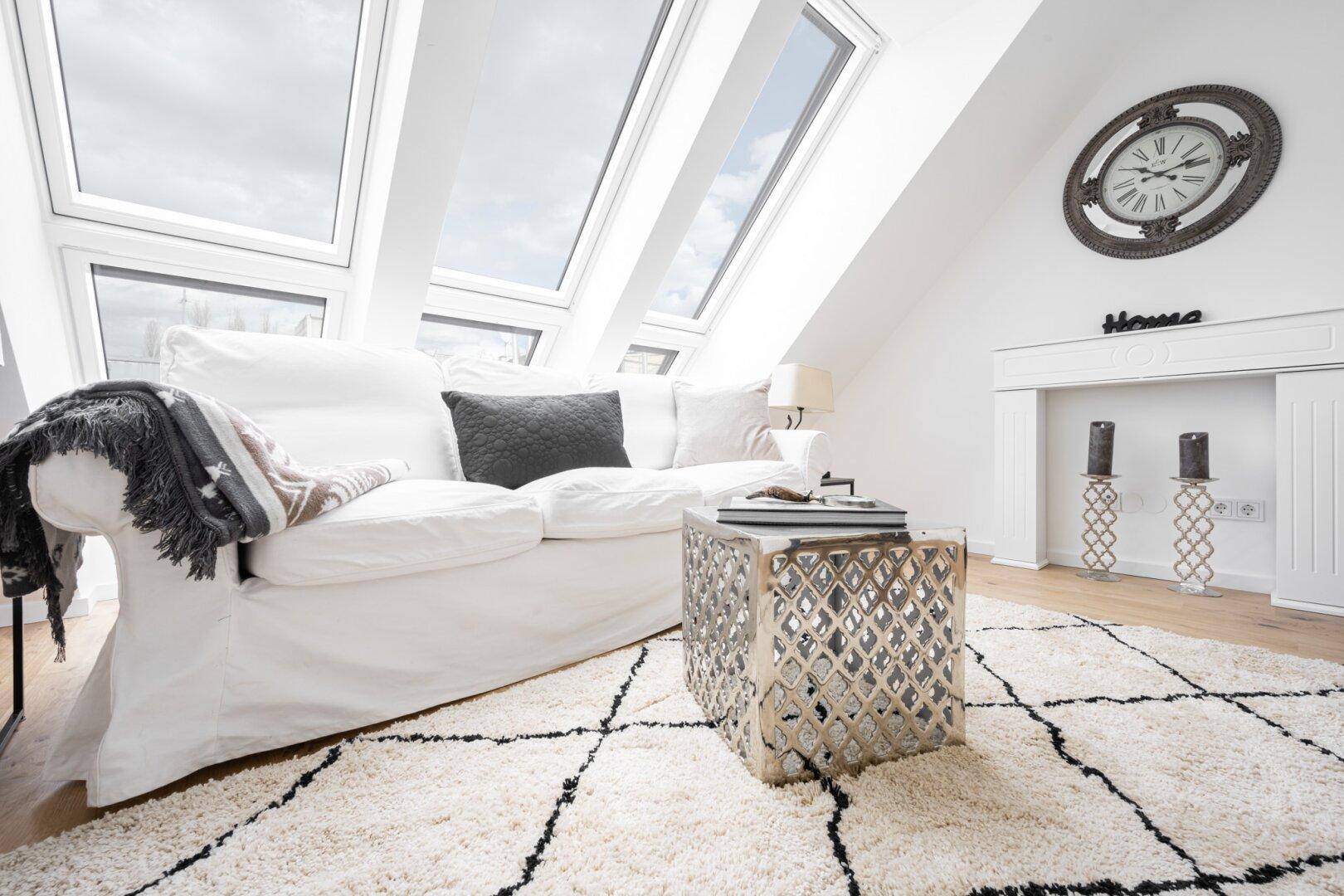 Geräumiger Wohnbereich mit weißer Couch, Teppich und viel Tageslicht durch die Dachfenster.