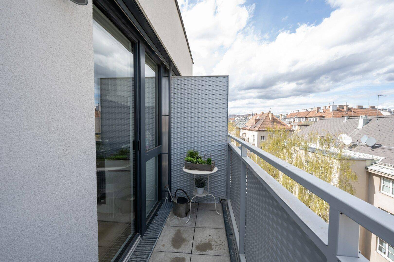 Kleiner Balkon mit Stadtblick, bepflanztem Tisch und moderner Brüstung.
