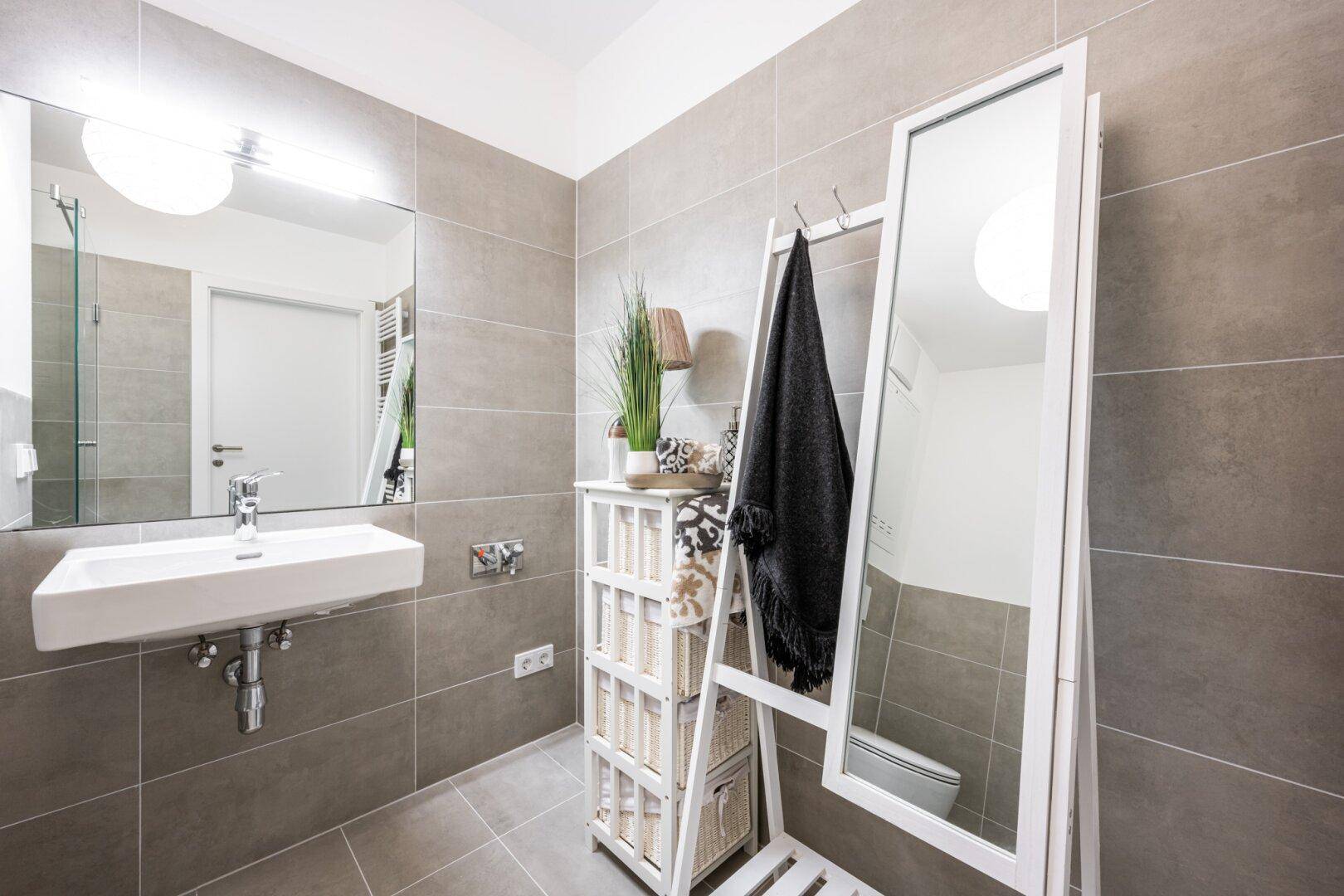Modernes Badezimmer mit grauen Fliesen, Einzelwaschbecken und einem großen Spiegel.