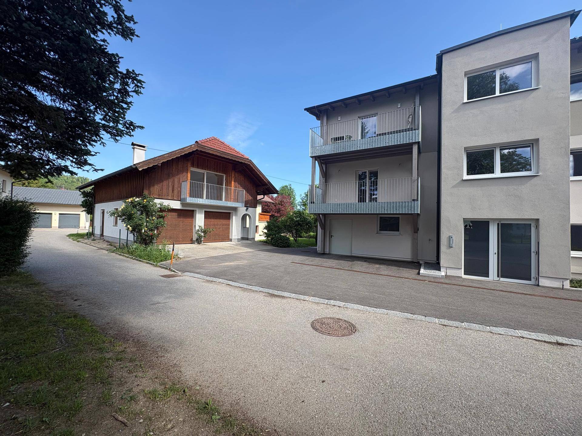 Gesamtansicht des traditionellen Hauses neben einem modernen Gebäude mit mehreren Balkonen und Zufahrt.