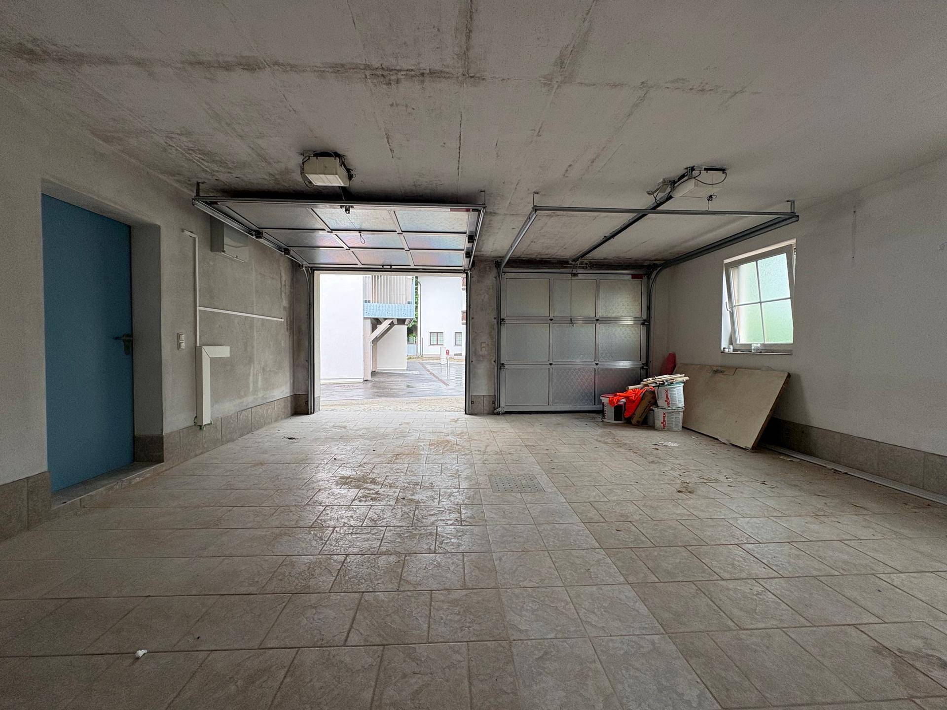 Geräumige Garage mit zwei Garagentoren, Fliesenboden und direktem Zugang zum Außenbereich.