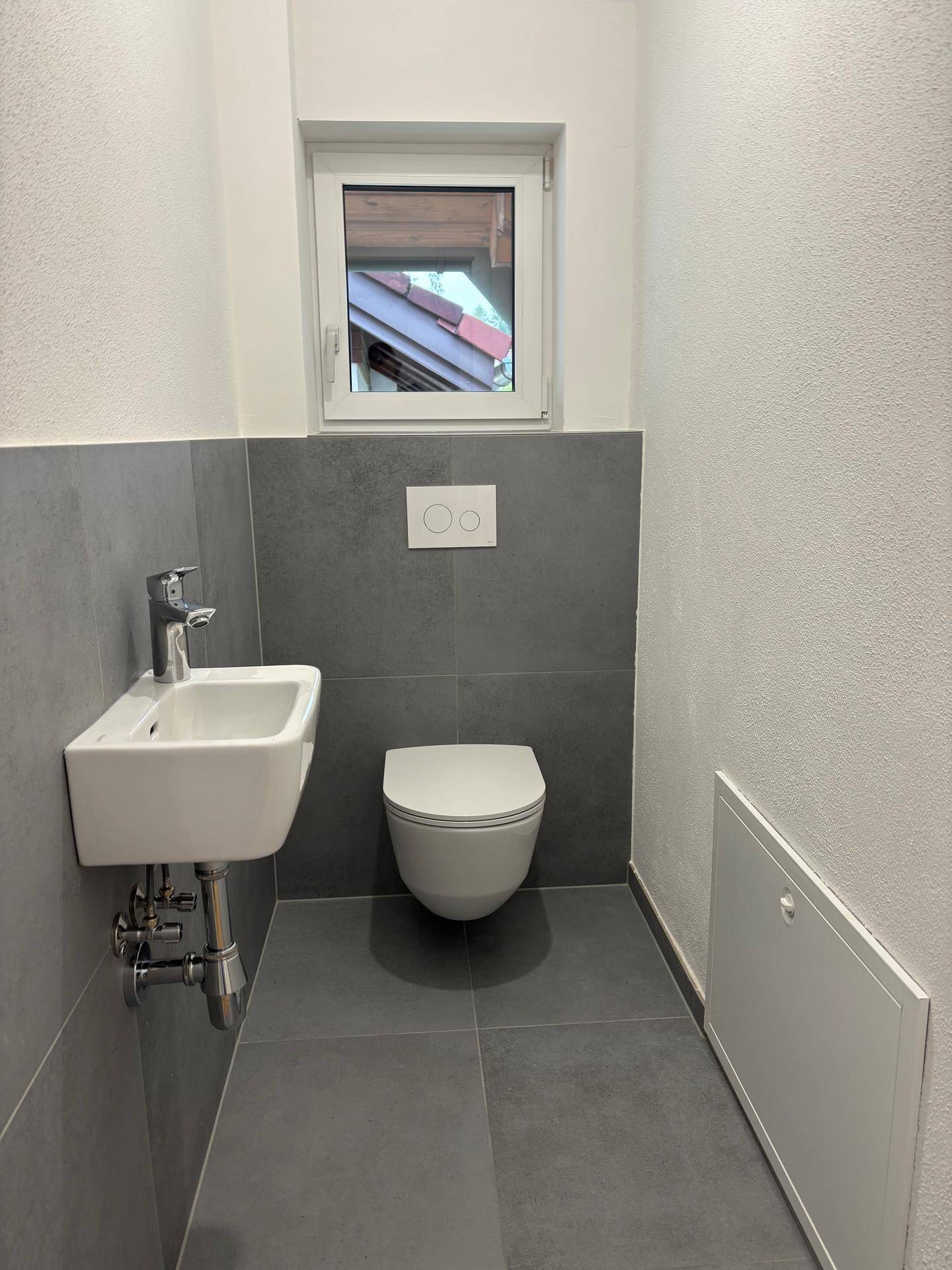 Gäste-WC mit wandhängender Toilette, kleinem Waschbecken und Fenster.