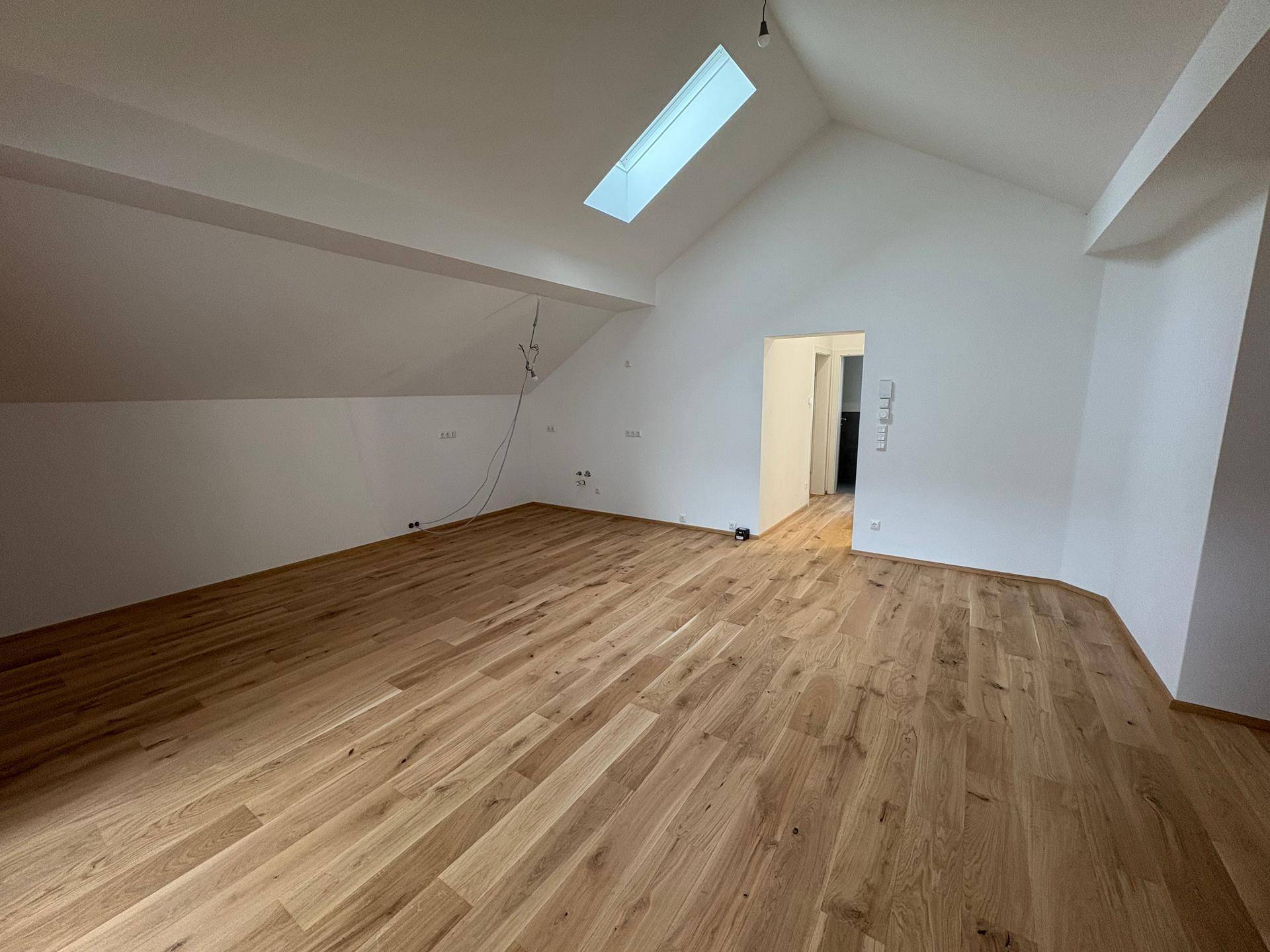 Heller Dachgeschossraum mit Holzboden, Dachfenster und schrägen Wänden.