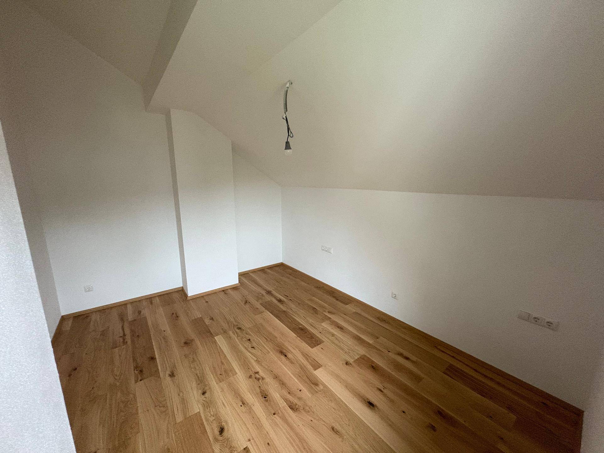 Helles Zimmer im Dachgeschoss mit Holzboden und weiß gestrichenen Wänden.