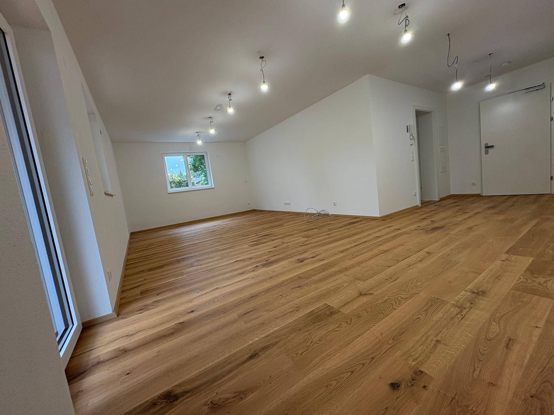 Geräumiger, unmöblierter Raum im Dachgeschoss mit Holzboden und schräger Decke.