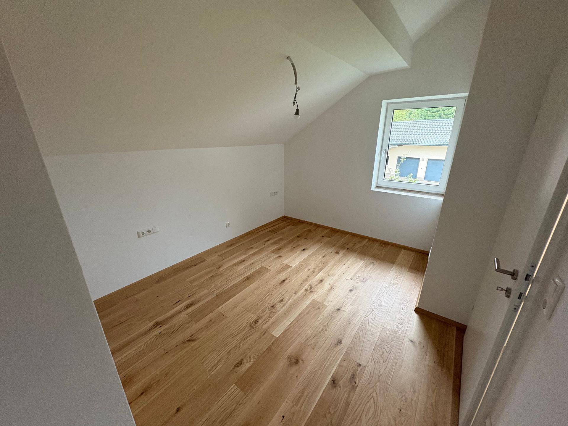 Schlafzimmer im Dachgeschoss mit Holzboden, Fenster und schrägen Wänden.