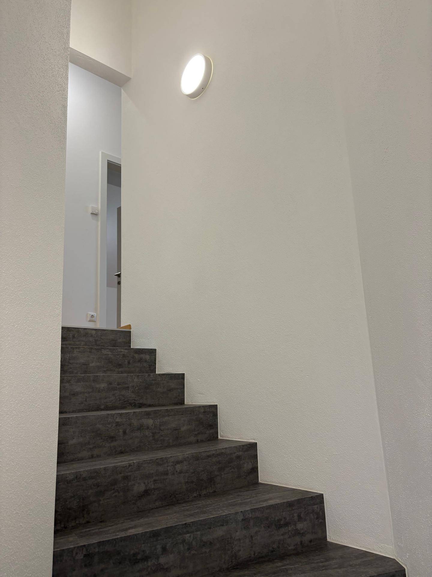 Treppenhaus mit schlichtem Design, weiß gestrichenen Wänden und Wandleuchte.
