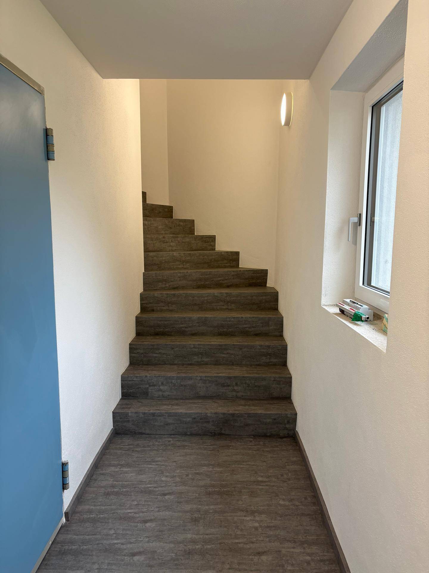 Heller Treppenaufgang mit modernem Bodenbelag und Fenster für natürliches Licht.