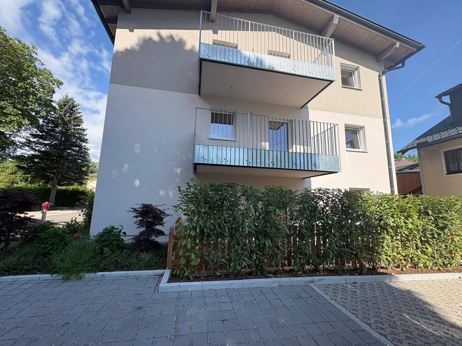 Fassade des Neubaus mit Balkonen und einer grünen Hecke im Vordergrund.