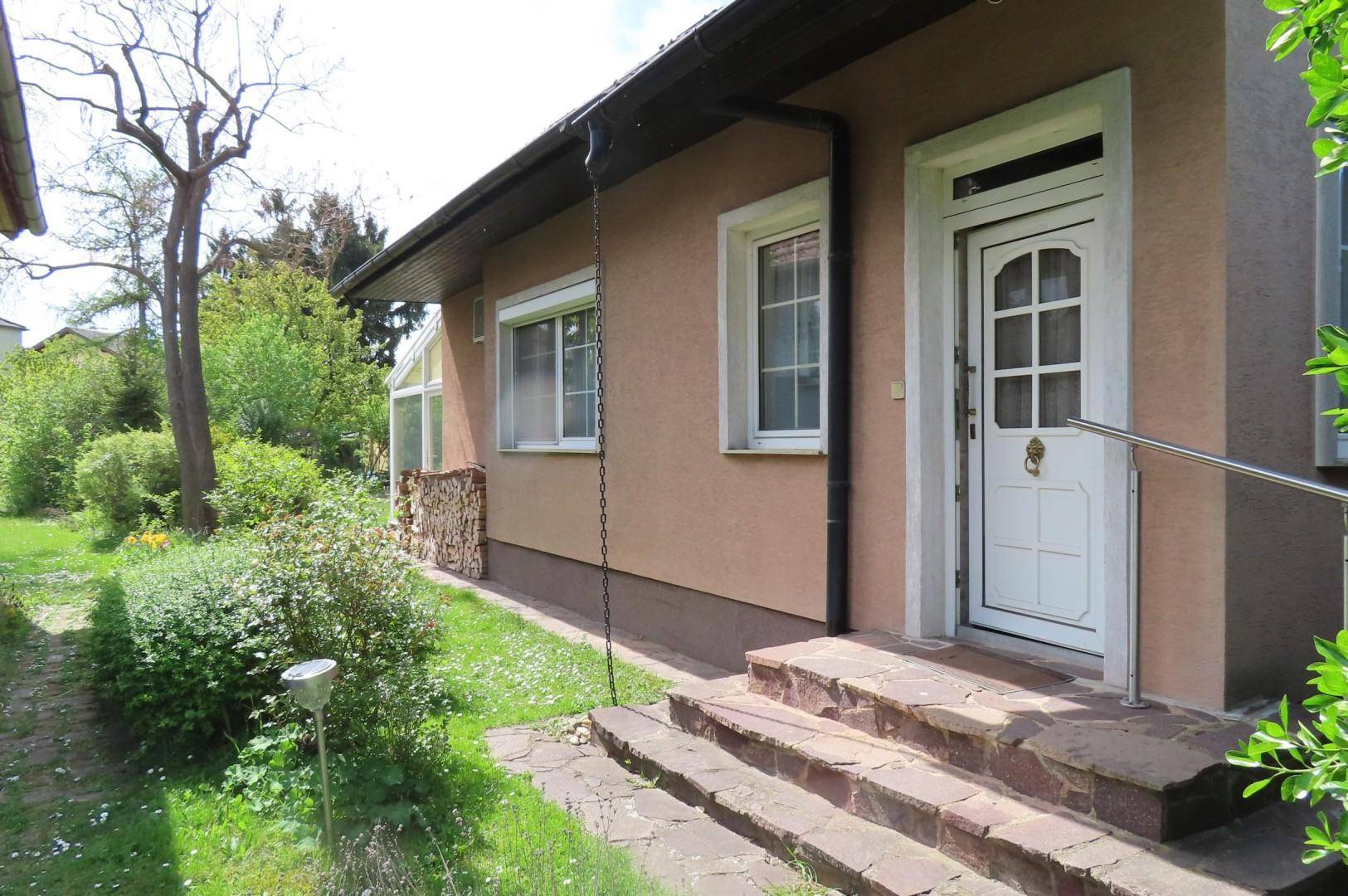 Eingangsbereich des Hauses mit weißer Tür, Steinstufen und einem kleinen Gartenweg.