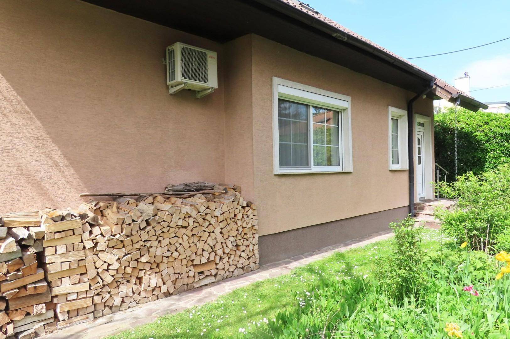 Seitenansicht des Hauses mit gestapeltem Brennholz, Klimaanlage und Fenster mit Rollladen.