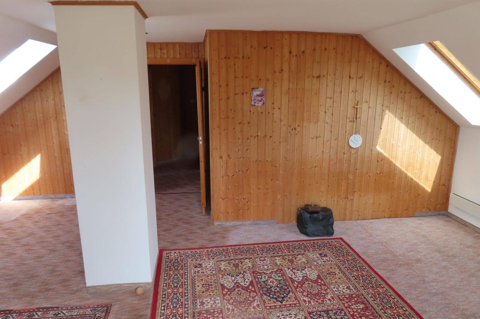 Ausbaufähiger Dachboden mit Holzverkleidung, Dachfenstern und Teppichboden.