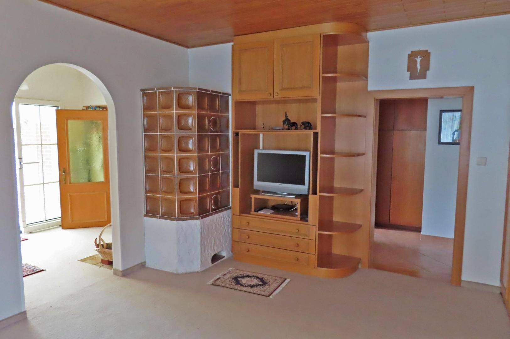 Wohnzimmer mit traditionellem Kachelofen, Holzmöbeln und einem Durchgang zu einem weiteren Raum.