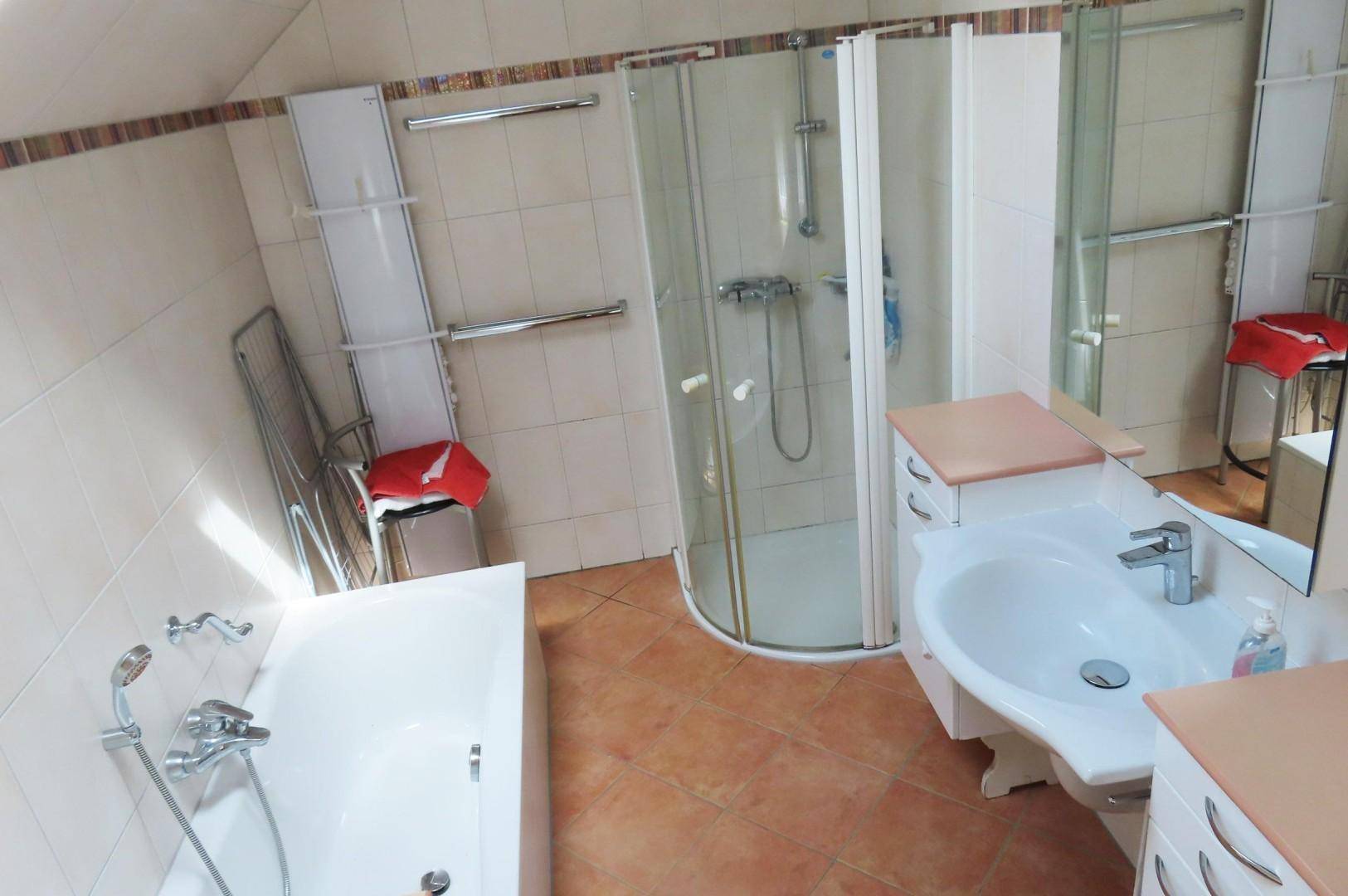 Badezimmer mit Badewanne, Eckdusche, Einzelwaschbecken und schrägen Wänden unter dem Dach.