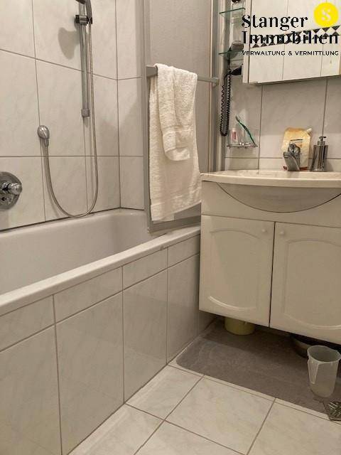 Badezimmer mit Badewanne, Duschfunktion und Waschbecken, komplett gefliest.