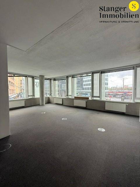 Weitläufiger Bürobereich mit durchgehender Fensterfront, grauem Teppich und viel Tageslicht.