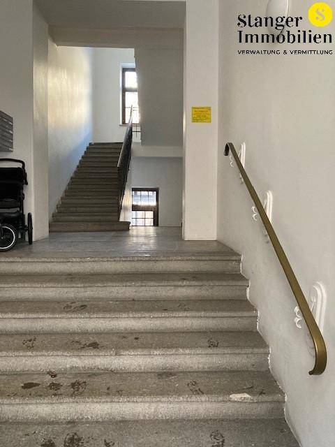 Heller Treppenaufgang mit Steinstufen und einem Handlauf an der Wand.