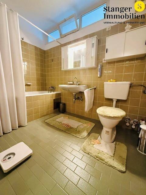 Badezimmer im 80er-Jahre-Stil mit Badewanne, Waschbecken, WC und Fliesenboden.
