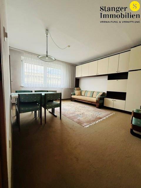 Geräumiges Wohn- und Esszimmer mit Teppichboden, großem Wandverbau und Fenster.