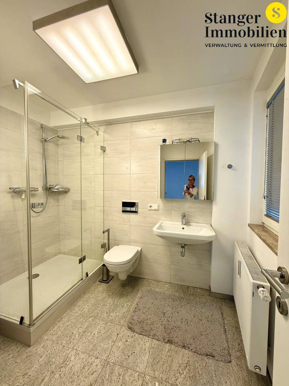 Modernes Badezimmer mit ebenerdiger Dusche, Hänge-WC und Waschbecken, auf hellen Fliesen.