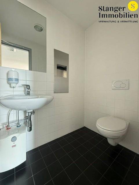 Helles Badezimmer mit weißen Fliesen, schwarzem Fliesenboden, Waschbecken und wandhängendem WC.