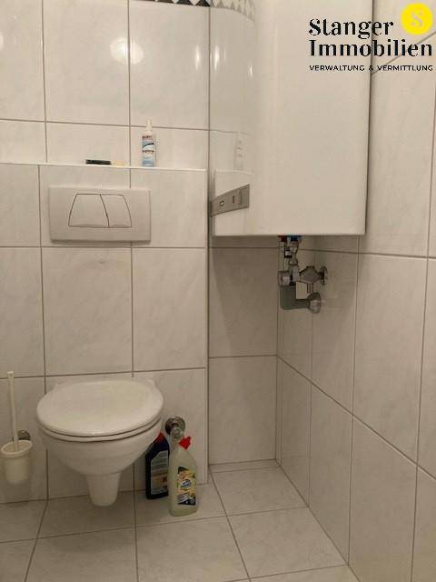 Separates WC mit wandhängender Toilette und Fliesen an Wänden und Boden.
