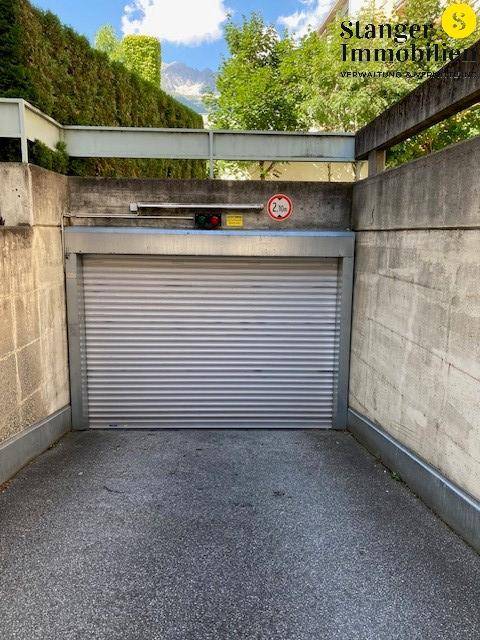Einfahrt zu einer Tiefgarage mit Rolltor, Höhenbegrenzungsschild und umgebender Betonstruktur.