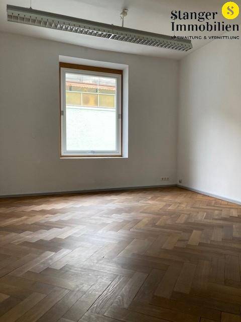 Heller Raum mit Fischgrätparkett und einem Fenster, das Tageslicht hereinlässt.