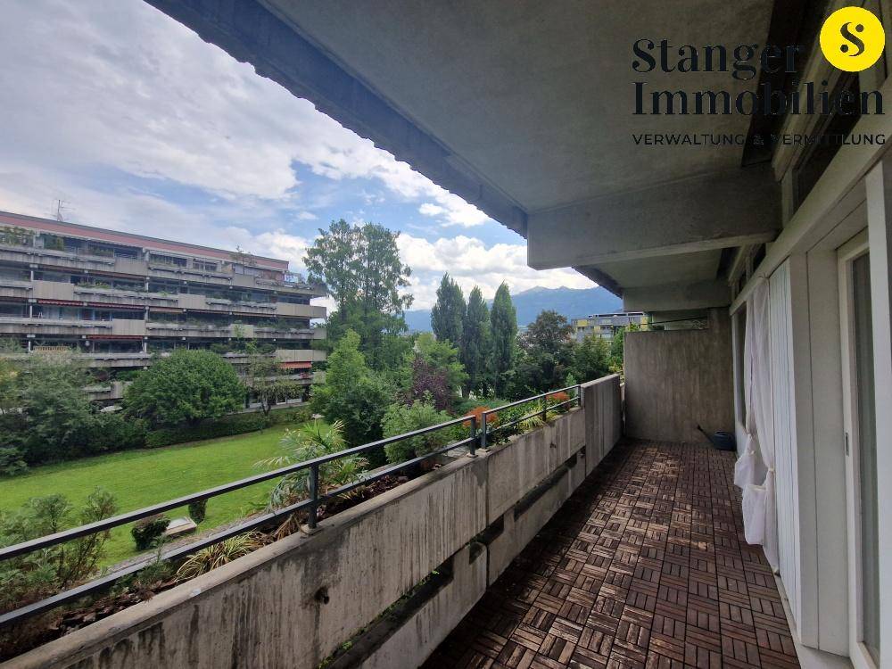 Langer Balkon mit Holzboden und Blick auf die grüne Umgebung und die umliegenden Gebäude.