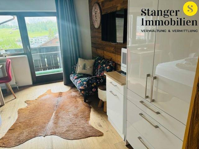 Wohnbereich mit floralem Sessel, Holzwand und einem modernen weißen Kleiderschrank mit Hochglanzfronten.