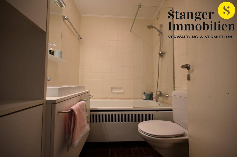 Helles Badezimmer mit Badewanne, Duschfunktion und WC, ausgestattet mit hellen Fliesen.