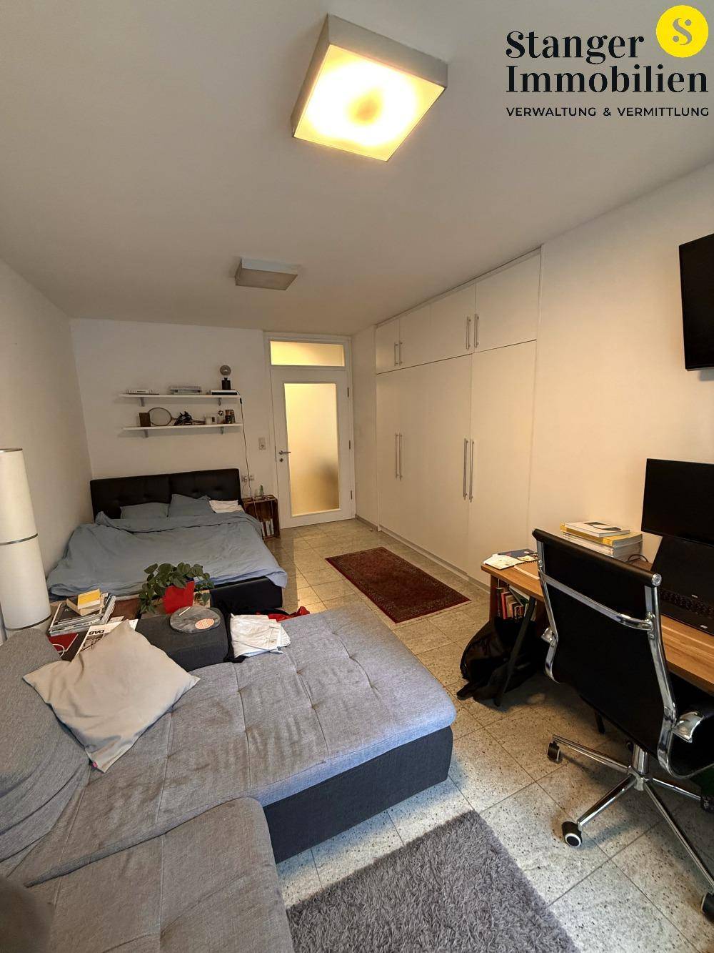 Schlafzimmer mit Bett, Sofa und Schreibtisch, ausgestattet mit Einbauschränken und Granitfliesenboden.