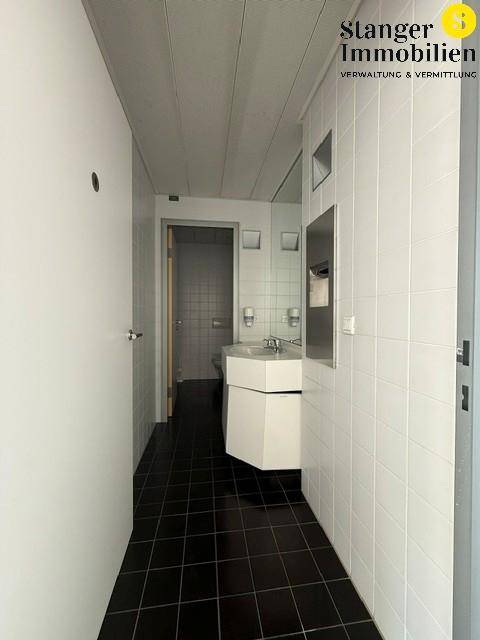 Schmaler Badezimmerbereich mit weißen Wandfliesen, dunklem Boden und einem modernen Waschtisch.