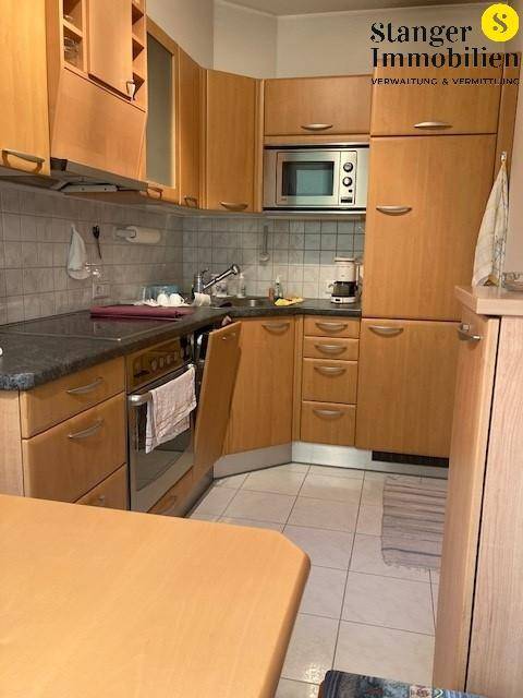 Funktionale Küche mit Holzschränken, dunkler Arbeitsplatte und integrierten Geräten.