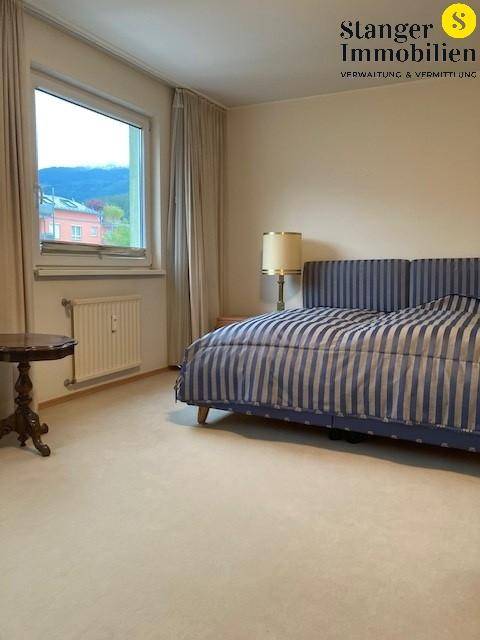 Schlafzimmer mit gestreiftem Bett, Teppichboden und Fenster mit Blick auf die Berge.