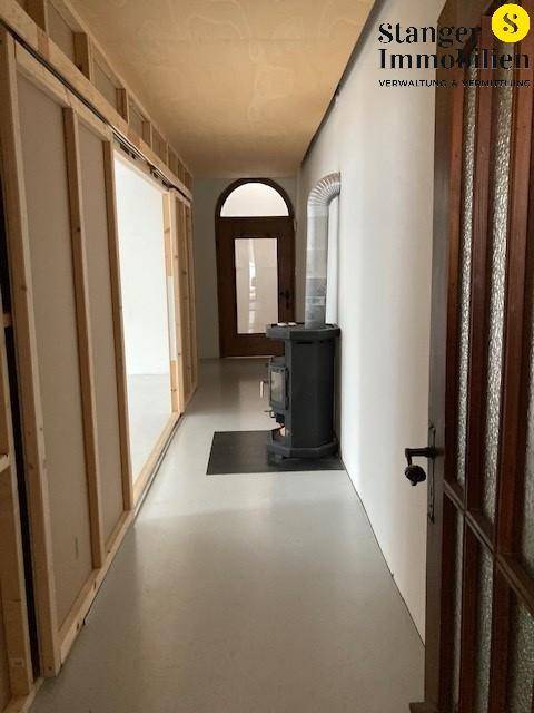 Langer Flur mit einem Holzofen, Schiebetüren und einer gewölbten Tür am Ende.