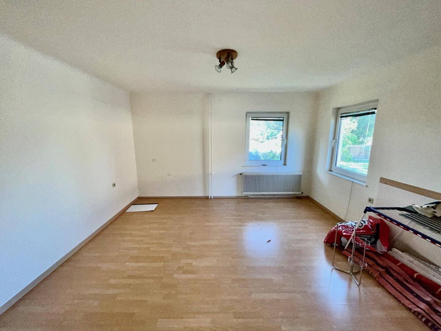 Helles, leeres Zimmer mit Holzparkettboden und zwei Fenstern, bereit zur individuellen Gestaltung.
