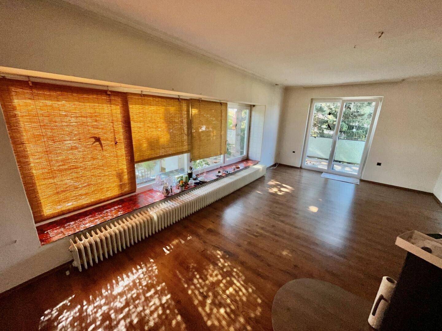 Helles Wohnzimmer mit breiter Fensterfront, Holzboden und direktem Zugang zum Balkon.