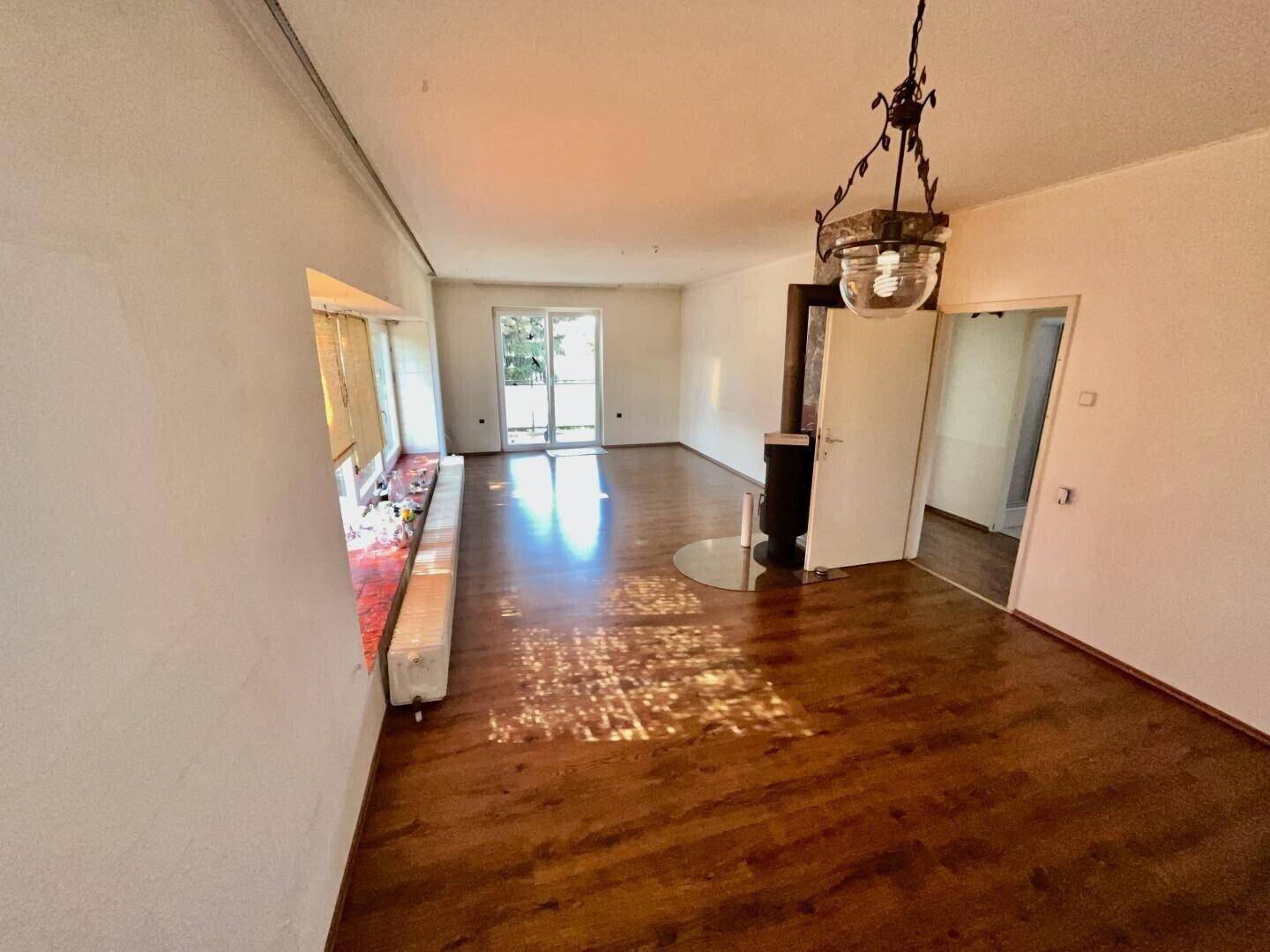 Lichtdurchflutetes Wohnzimmer mit Kaminofen, Holzboden und Zugang zum Balkon.